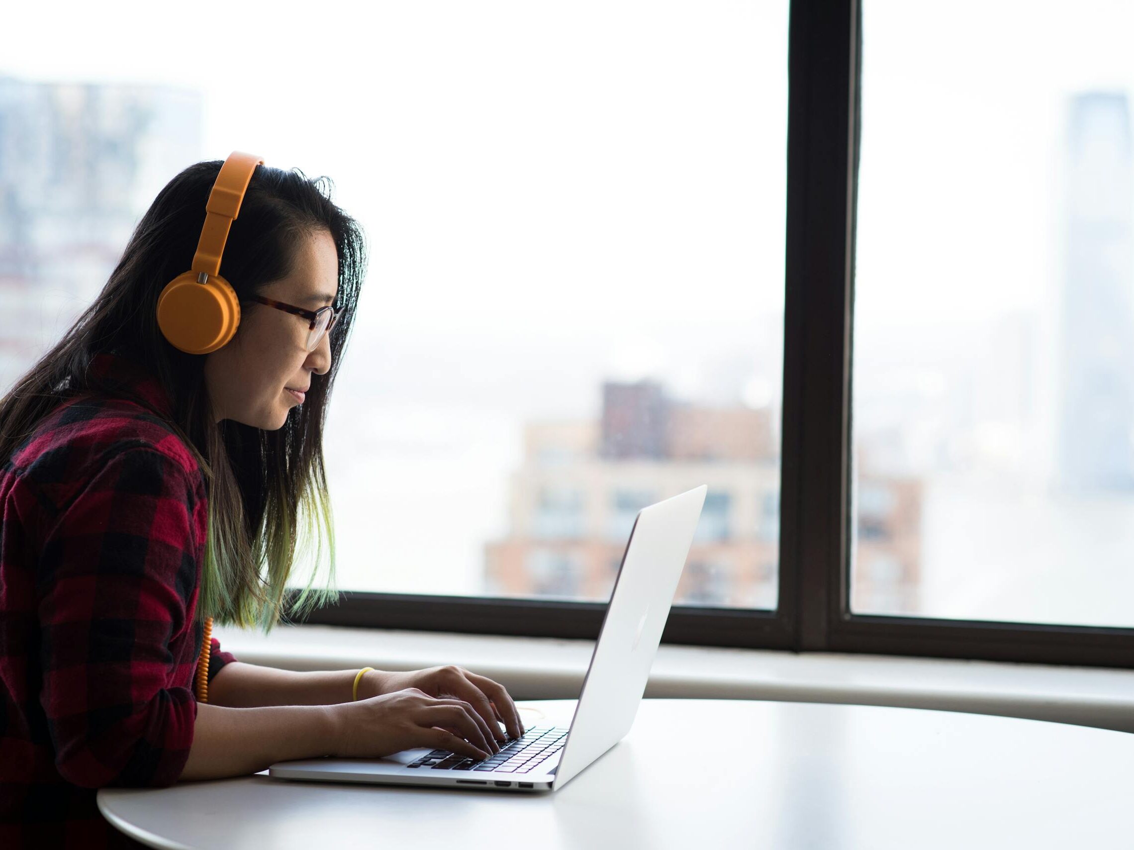 Asian woman with headphones using laptop for remote work in a city setting.