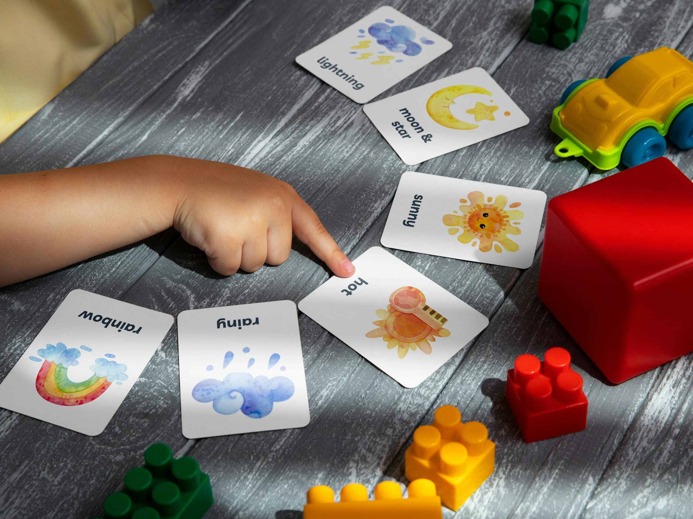 Close-up of a child pointing at colorful educational flashcards and toys, promoting learning and creativity.