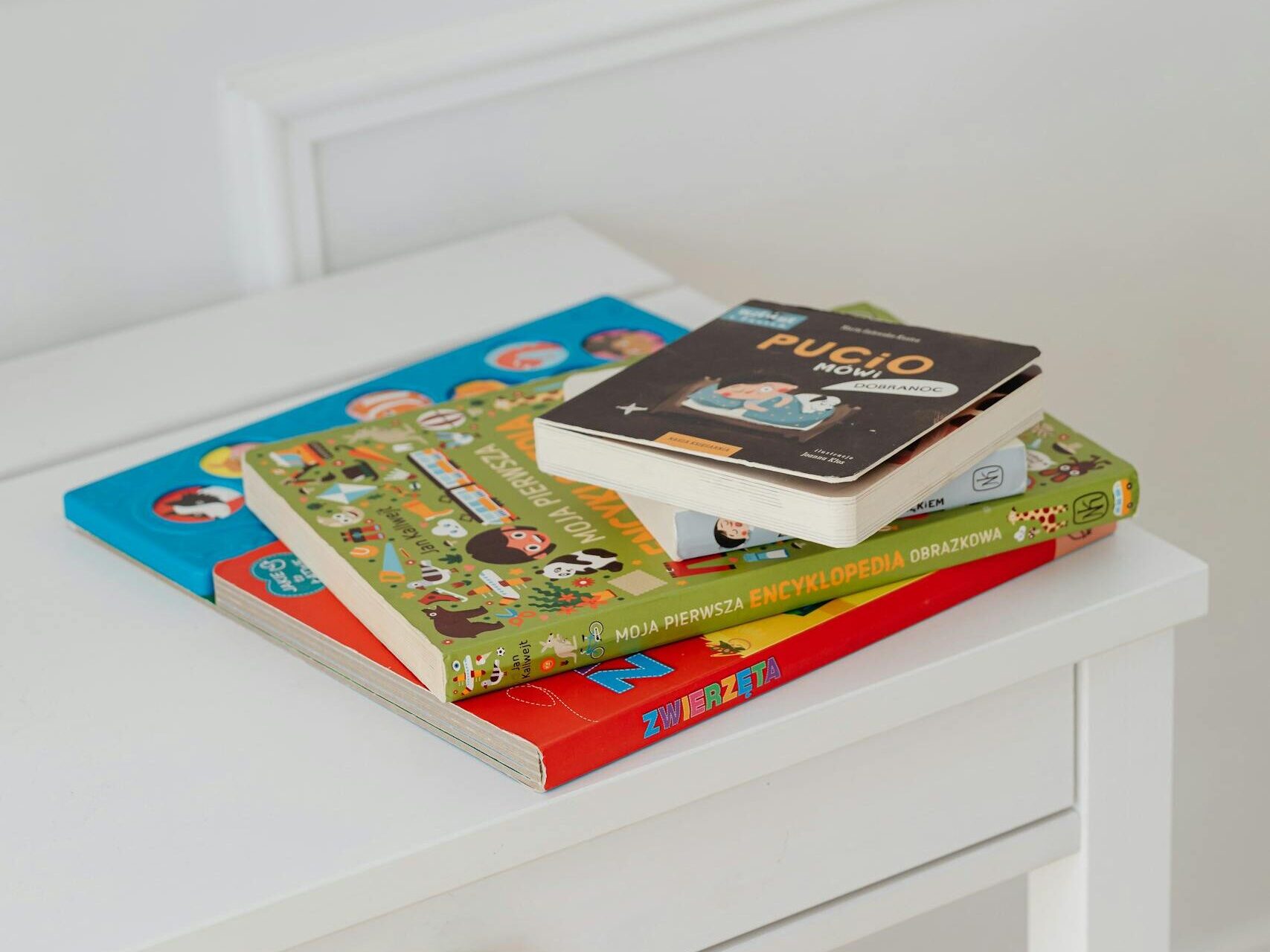 Vertical shot of children's books stacked on a white table in a bright space.